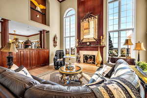 Living area featuring ornamental molding, wood finished floors, decorative columns, a premium fireplace, and a high ceiling