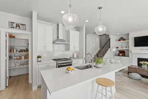 Kitchen featuring open floor plan, stainless steel range with gas cooktop, a fireplace, white cabinets, and light wood finished floors