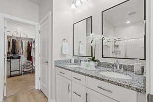 Full bath featuring double vanity, a walk in closet, a shower stall, and light wood-style flooring