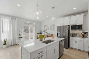 Kitchen featuring white cabinets, hanging light fixtures, a kitchen island with sink, stainless steel appliances, and light wood-type flooring