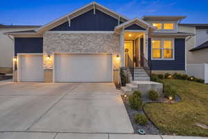 View of front facade featuring a garage, stone siding, driveway, a front lawn, and board and batten siding