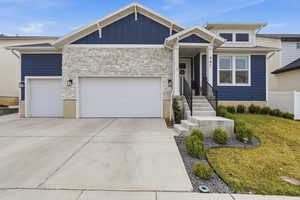 View of front facade featuring an attached garage, stone siding, driveway, a front lawn, and board and batten siding
