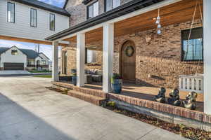 View of exterior entry featuring brick siding, a porch, and driveway