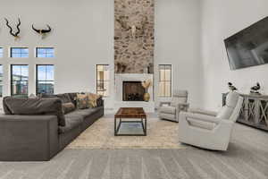 Carpeted living room featuring a high ceiling and a stone fireplace