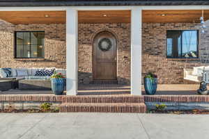 View of exterior entry featuring covered porch, brick siding, and outdoor furniture