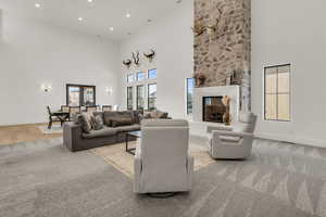 Living room featuring light colored carpet, a high ceiling, a stone fireplace, and recessed lighting