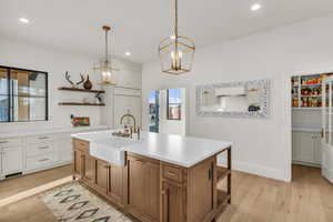 Dual tone kitchen with two tone color scheme, open shelves, a kitchen island with sink, light wood-style floors, and a chandelier