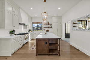 Kitchen with open shelves, a chandelier, a kitchen island with sink, two tone cabinets, and light wood-style floors