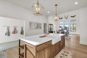 Kitchen with light wood-style flooring, a chandelier, a center island with sink, and a high ceiling