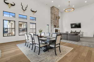 Dining room with a high ceiling, a large fireplace, light wood-style floors, and a chandelier