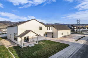 Rear view of house featuring a mountain view, a patio, a lawn, a residential view, and a shingled roof