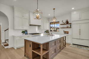 Kitchen with open shelves, high end appliances, two tone cabinets, arched walkways, and a center island with sink