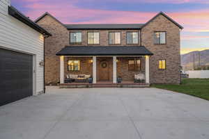 Traditional home with a porch, a mountain view, driveway, brick siding, and a yard