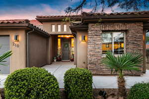 Exterior entry at dusk featuring stone siding, stucco siding, a garage, and a tiled roof