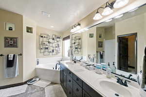 Full bathroom featuring double vanity, a garden tub, a textured ceiling, and light tile patterned flooring
