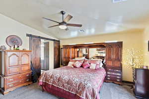 Bedroom featuring a barn door, carpet floors, and a ceiling fan