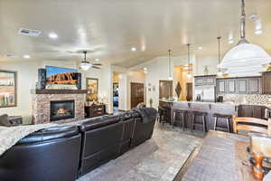 Living area featuring ceiling fan, lofted ceiling, a stone fireplace, and recessed lighting