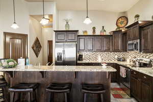 Kitchen featuring dark wood finish cabinetry, stainless steel appliances, a kitchen bar, and light stone countertops