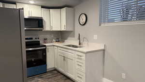Kitchen featuring stainless steel appliances, white cabinets, light stone counters, and dark wood-style flooring