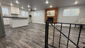 Living area featuring a ceiling fan, a large fireplace, dark wood-style flooring, recessed lighting, and a textured ceiling