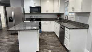 Kitchen with dark stone counters, stainless steel appliances, a center island, dark wood-type flooring, and white cabinetry