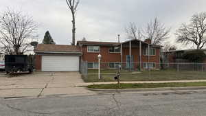 Split foyer home featuring a garage, brick siding, driveway, a fenced front yard, and a chimney