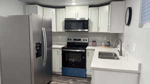 Kitchen with stainless steel appliances, light stone counters, white cabinetry, dark wood-style floors, and a textured ceiling