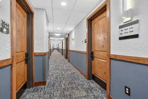 Corridor with a textured wall, dark colored carpet, and recessed lighting