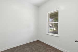 Empty room featuring baseboards and dark carpet