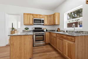 Kitchen with stainless steel appliances, dark stone countertops, light wood-style flooring, and a peninsula
