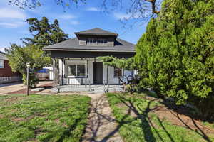 Bungalow-style home featuring covered porch, a shingled roof, and a front yard