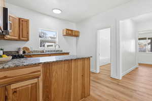Kitchen featuring dark stone counters, light wood finished floors, stainless steel microwave, wood finish cabinets, and a peninsula