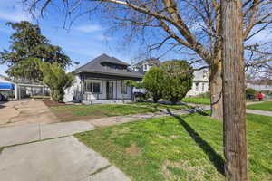 Bungalow-style house with covered porch, roof with shingles, a front lawn, and driveway