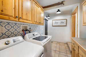 Laundry room featuring cabinet space, washing machine and clothes dryer, and light stone finish floors