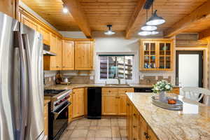 Kitchen with stainless steel appliances, light stone countertops, a wood ceiling with exposed beams, decorative light fixtures, and glass fronted cabinets