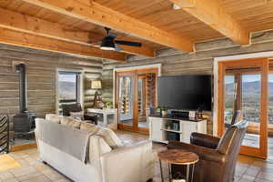 Living area with log walls, a wooden ceiling with exposed beams, a wood stove, and ceiling fan
