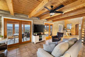Living room with french doors, plenty of natural light, a wooden ceiling with exposed beams, and log walls
