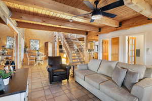 Living room featuring a wooden ceiling with exposed beams, arched walkways, stone tile floors, wood walls, and a ceiling fan