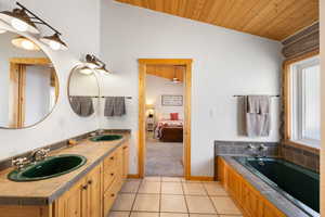Bathroom featuring ensuite bath, a vaulted wooden ceiling, double vanity, a bath, and light tile patterned floors