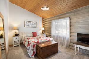 Bedroom featuring log walls, a vaulted wood ceiling, and carpet