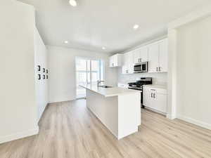 Kitchen featuring stainless steel appliances, light wood finished floors, white cabinetry, an island with sink, and recessed lighting