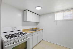 Kitchen featuring gas range gas stove, white cabinets, a textured ceiling, and light floors
