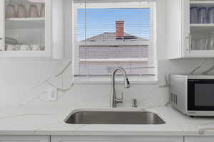 Kitchen view of light stone counters, white cabinetry, stainless steel microwave, and decorative backsplash