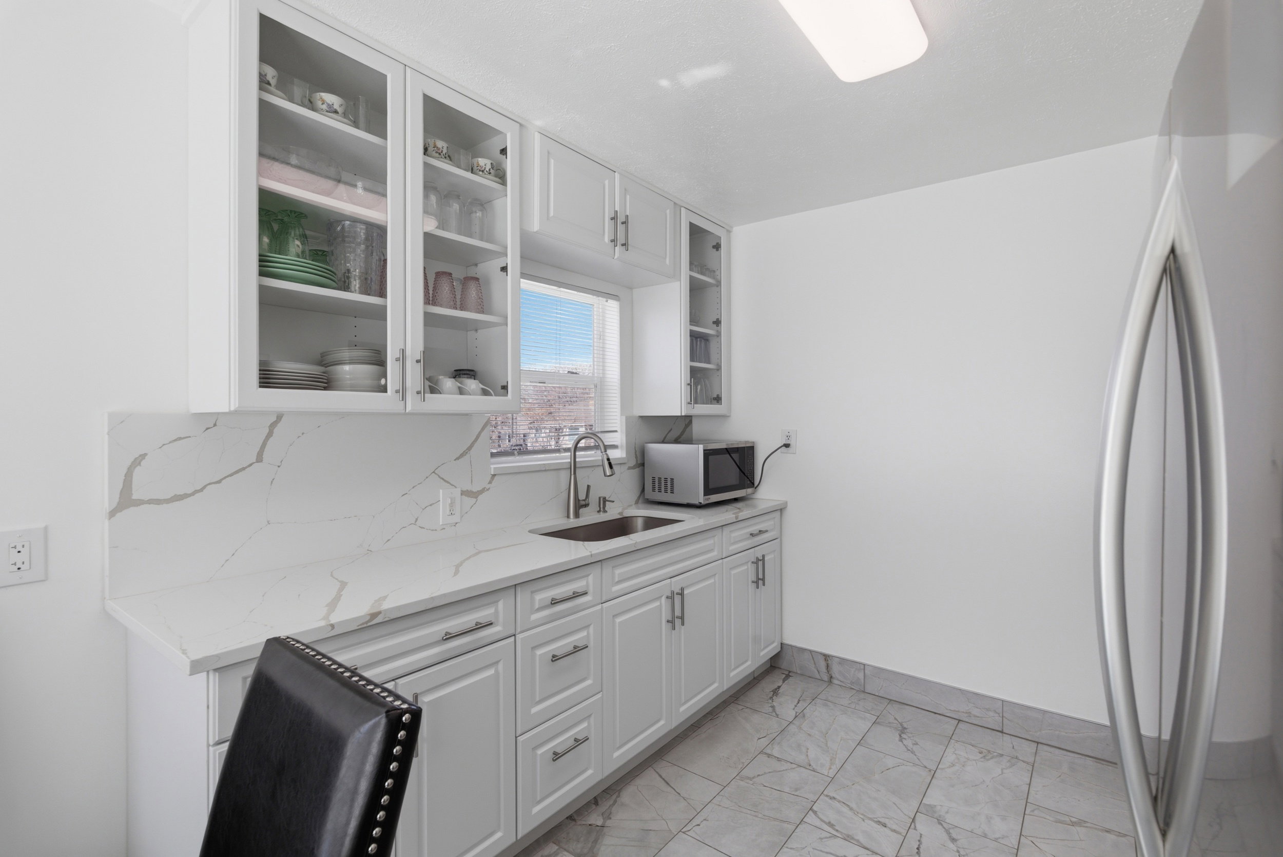 Kitchen featuring stainless steel appliances, light stone countertops, white cabinetry, glass fronted cabinets, and light marble finish floors