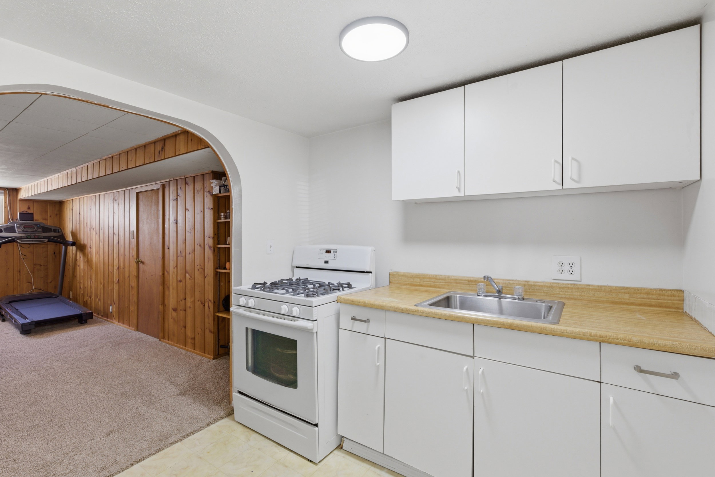 Kitchen featuring gas range gas stove, light countertops, white cabinets, arched walkways, and wood walls