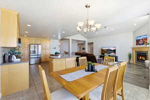 Dining area featuring a fireplace with flush hearth, hanging lights, light tile patterned floors, and lofted ceiling