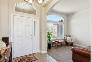 Foyer entrance with light carpet, hanging lights, light tile patterned flooring, and arched walkways