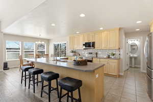 Kitchen featuring stainless steel appliances, a chandelier, dark countertops, a kitchen island with sink, and a breakfast bar area
