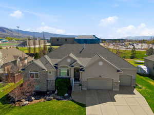 View of front of property featuring a mountain view, an attached garage, stone siding, stucco siding, and a front lawn