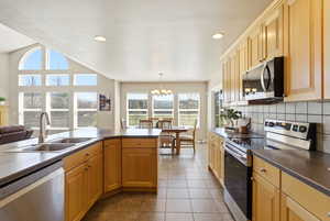 Kitchen with stainless steel appliances, dark countertops, light tile patterned flooring, suspended lighting, and tasteful backsplash